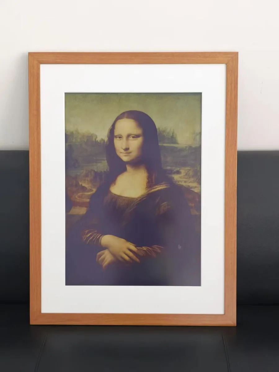 A colour E-Ink panel in a wooden frame with a white mat displaying the Mona Lisa